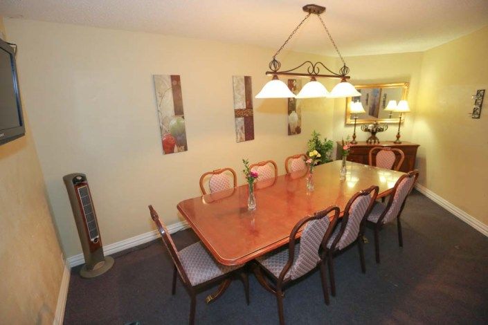 A spacious dining room with a large wooden table and chairs, illuminated by a stylish chandelier.