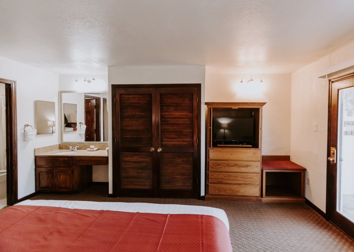 A cozy hotel room with wooden furniture, a television, and a mirror.