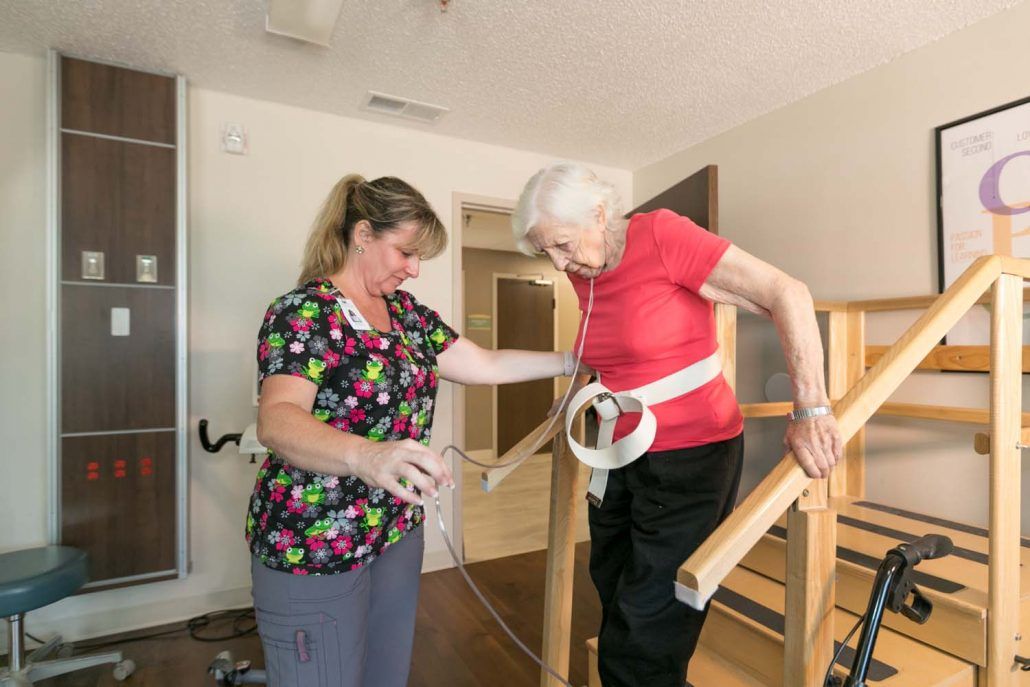 A caregiver assists an elderly woman during a physical therapy session.