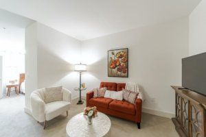A cozy living room featuring a red sofa, white armchair, floor lamp, coffee table with decor, and wall artwork.