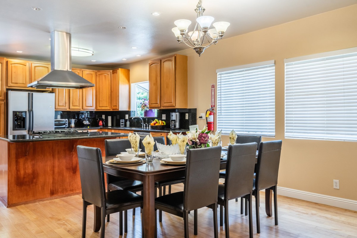 A modern open-concept dining area connected to a kitchen, featuring a stylish chandelier and elegant table settings.
