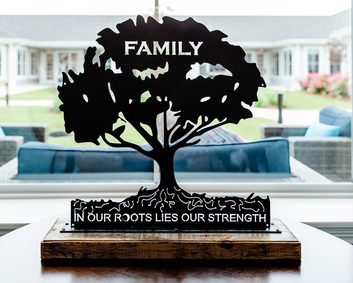 A decorative sign featuring a tree silhouette with the words 'FAMILY' and 'In our roots lies our strength'.