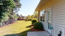 A sunny day view of a house with a spacious yard, surrounded by grass and bushes.