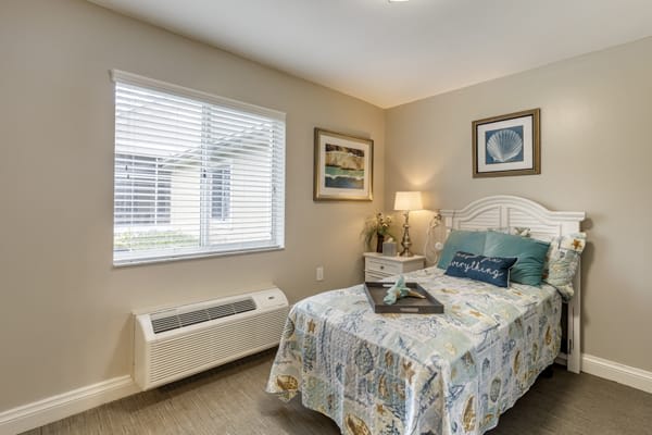A cozy bedroom with a neatly made bed, framed artwork, and a warm lighting ambiance.
