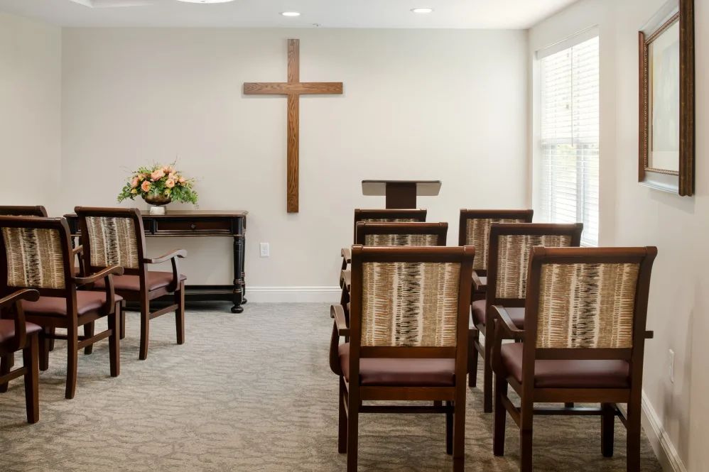 A small chapel with rows of chairs facing a cross on the wall, ready for a religious service.