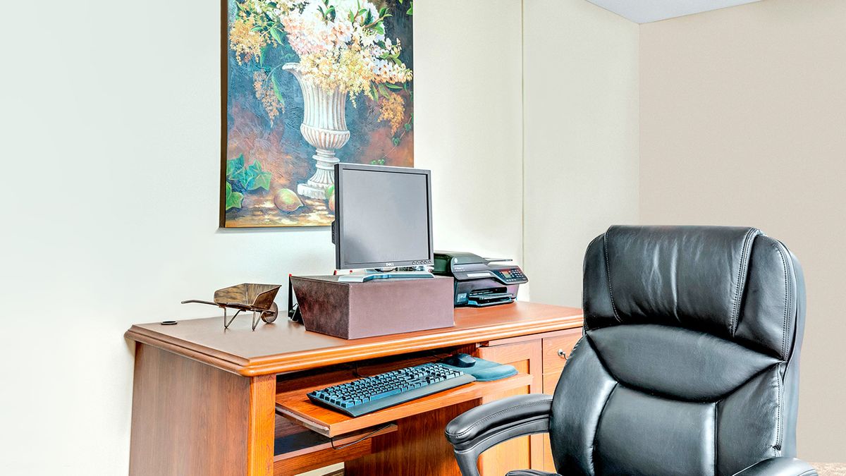 An organized office workspace with a desk, computer, and a painting on the wall.