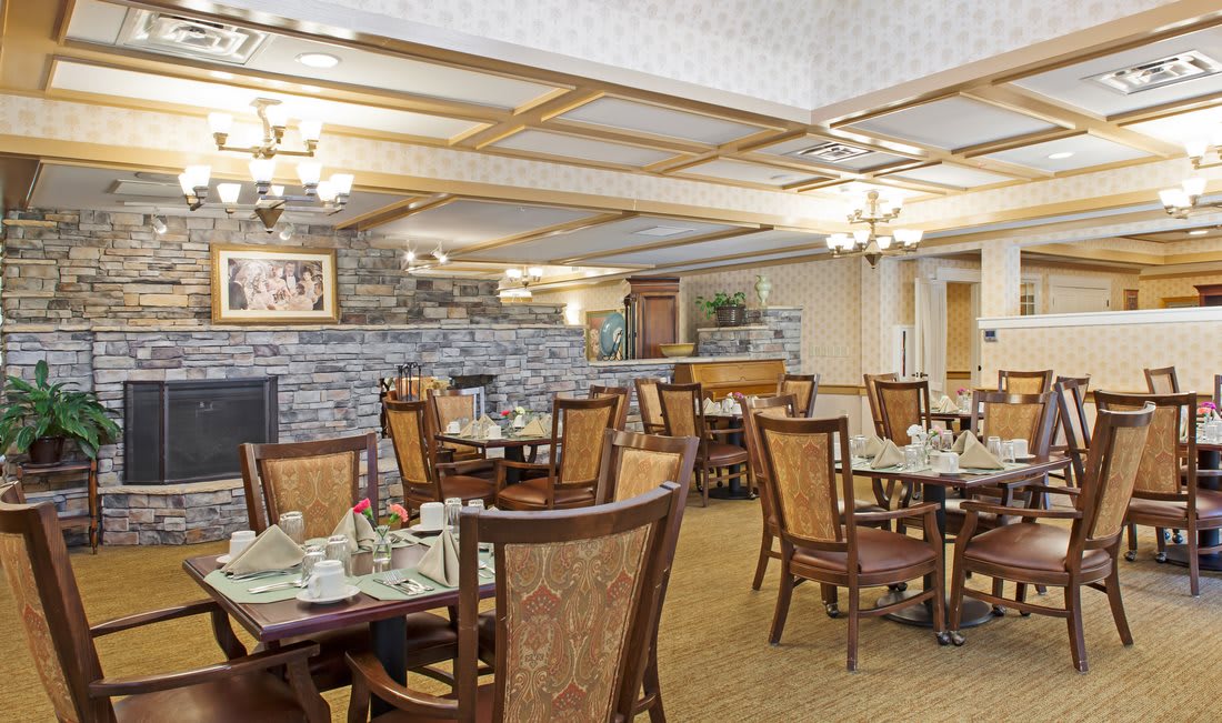 A cozy and elegant dining area with neatly arranged tables and chairs, featuring warm lighting and stone wall accents.