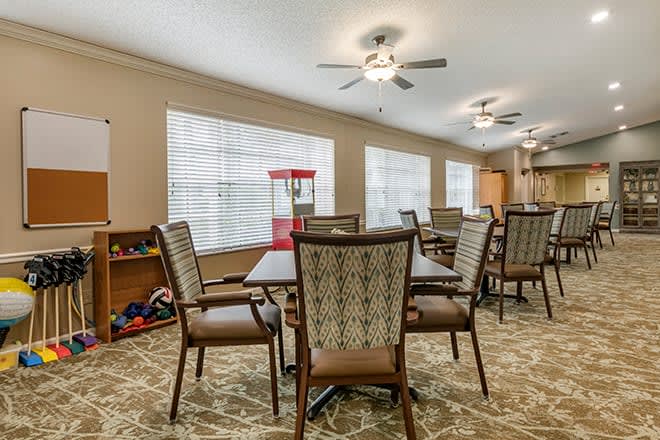 A well-lit dining area featuring multiple tables and chairs, complemented by large windows and ceiling fans.