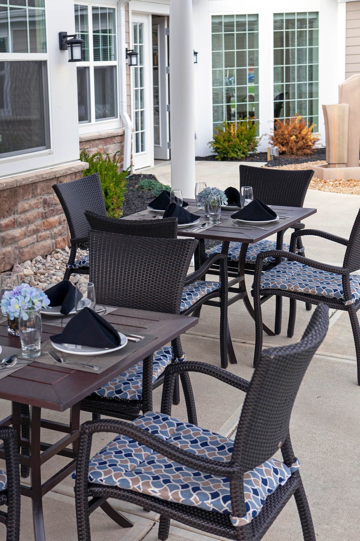An outdoor restaurant patio with elegantly set tables and chairs, featuring black napkins and glassware.