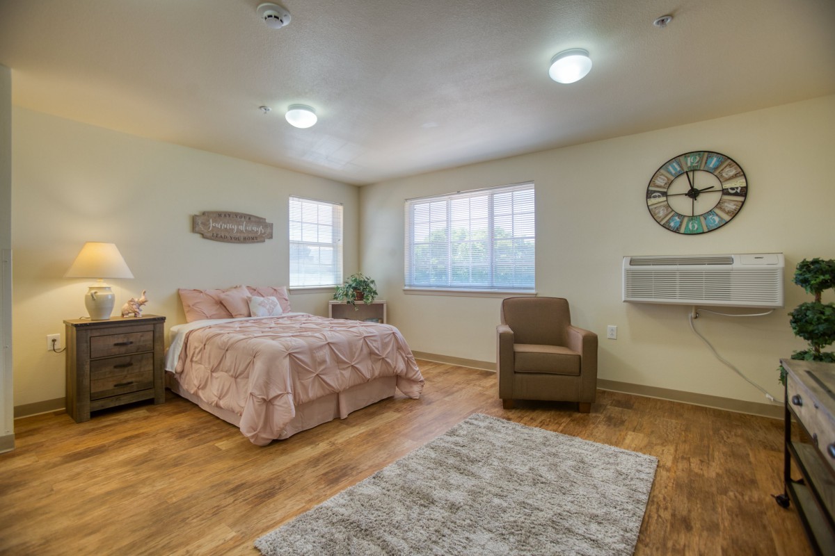 A cozy bedroom featuring a bed, armchair, and large windows.