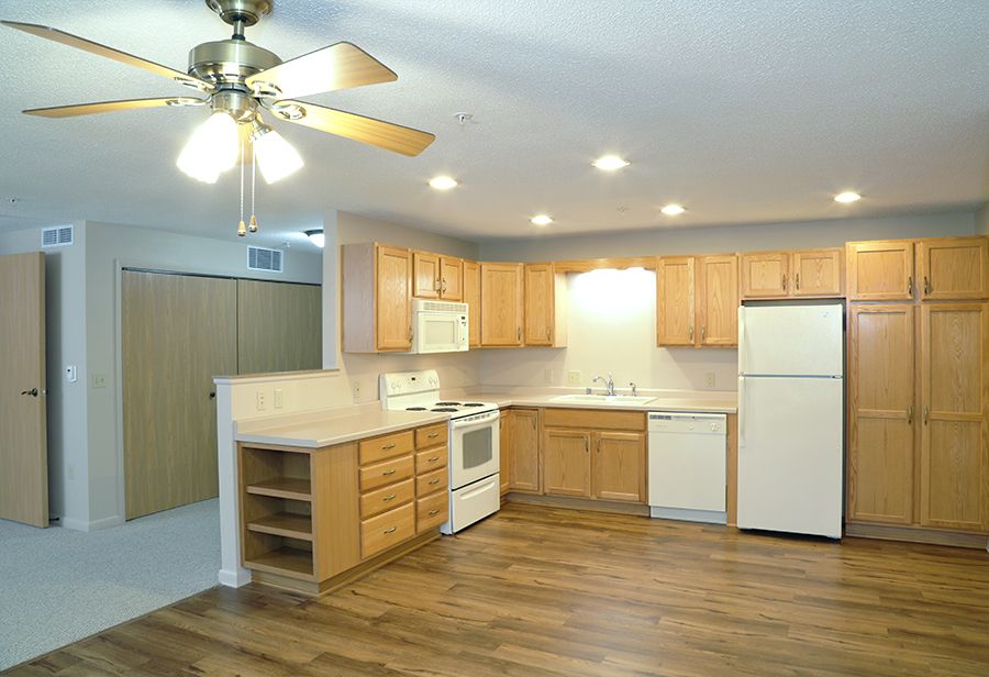 A modern kitchen with wooden cabinets, a ceiling fan, and various appliances including a white refrigerator and stove.
