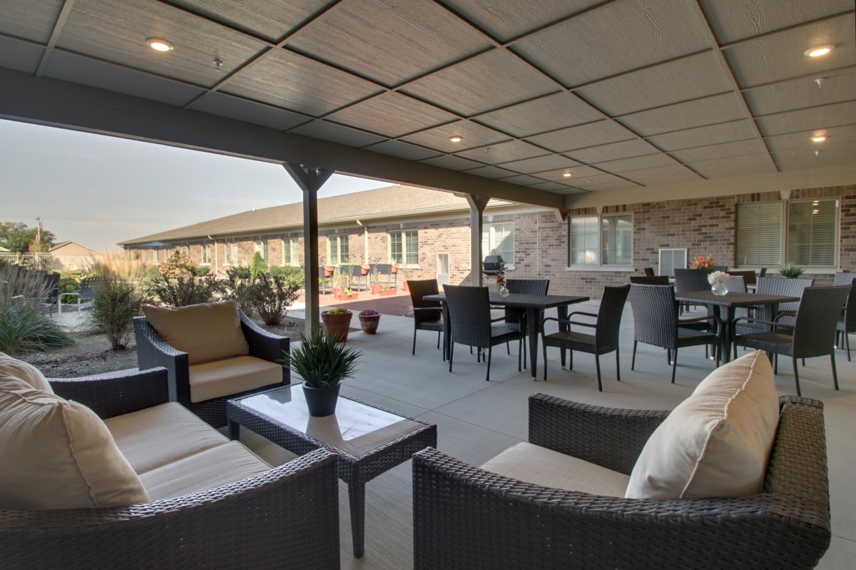 A covered outdoor patio with comfortable seating and a dining area, surrounded by plants.