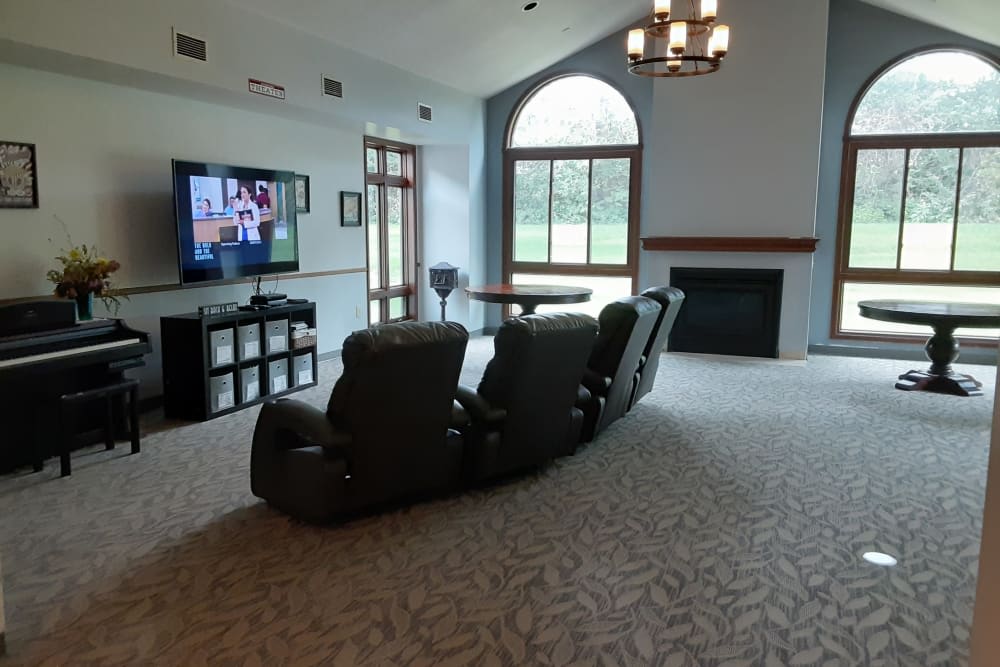 A spacious living room featuring a home theater setup with recliner chairs and a large television, complemented by a fireplace and a large arched window.