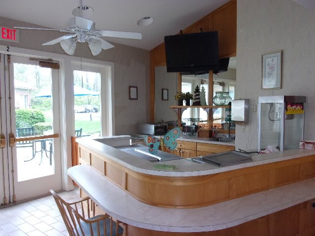 A cozy kitchen with a bar counter, ceiling fan, and television.