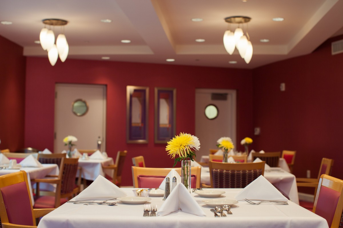 A neatly set dining area with tables adorned with flowers and folded napkins.