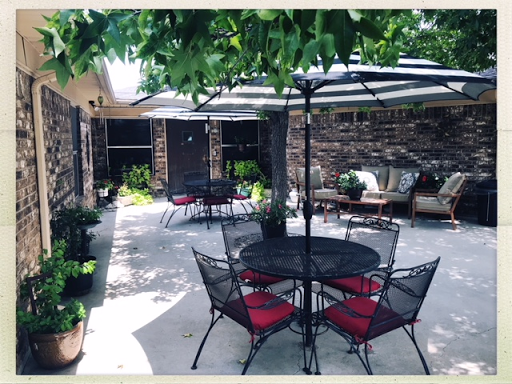 A serene outdoor patio area featuring black iron furniture with red cushions, surrounded by lush greenery.
