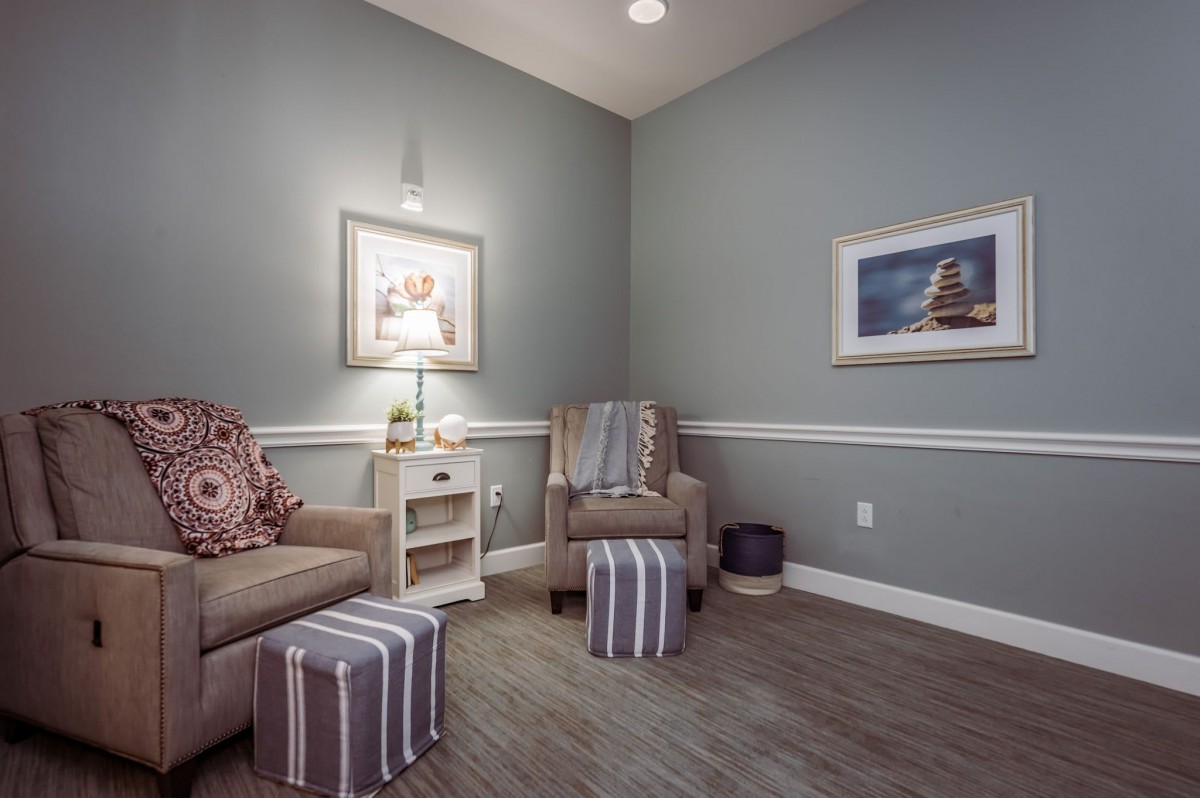 A cozy living room with an armchair, ottoman, and warm lighting.