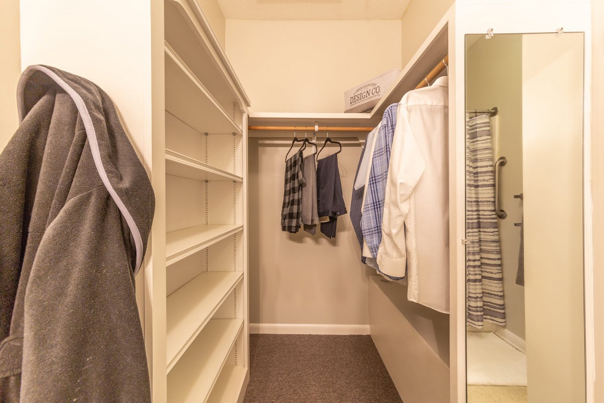 A tidy walk-in closet with hanging clothes and empty shelves ready for use.