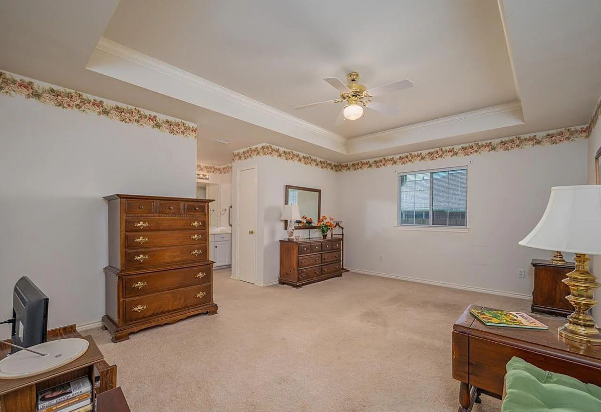 A spacious bedroom with traditional furniture, featuring a dresser and a chest of drawers under a ceiling fan.