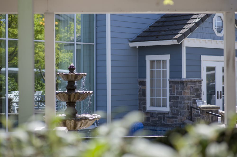 A view of a fountain and the exterior of a blue house with a window, partially obscured by foliage.