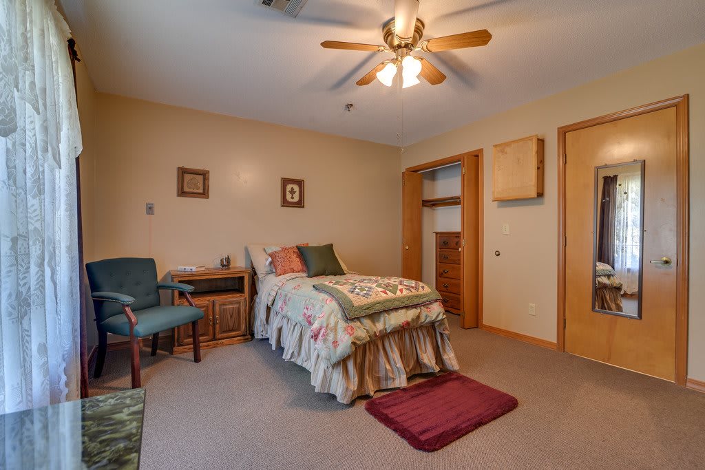 A cozy bedroom with a single bed, ceiling fan, and carpeted floor.
