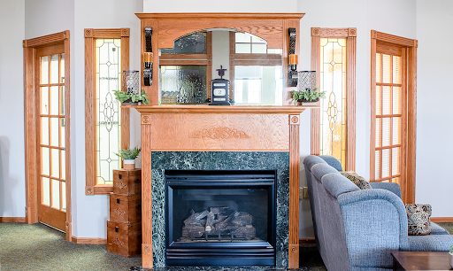 A beautifully designed fireplace with a wooden mantle and green marble base, illuminated by natural light from two windows.