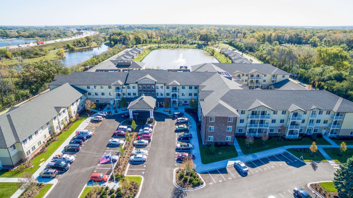 Aerial view of a residential complex with a parking lot and a pond surrounded by trees.