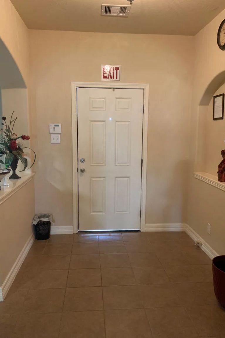 A hallway with a door and an exit sign above, featuring decorative plants on either side.