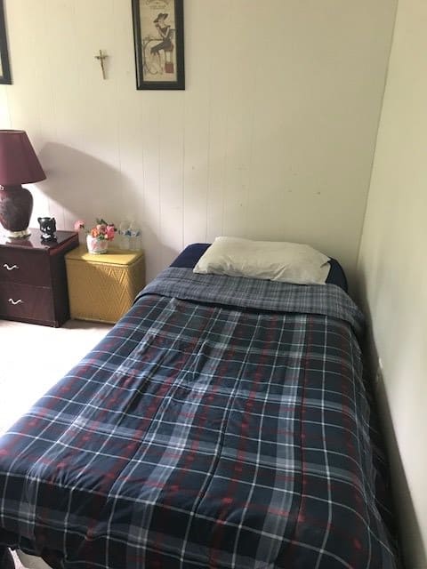 A cozy bedroom with a neatly made single bed featuring a plaid blanket, alongside a nightstand with a lamp.
