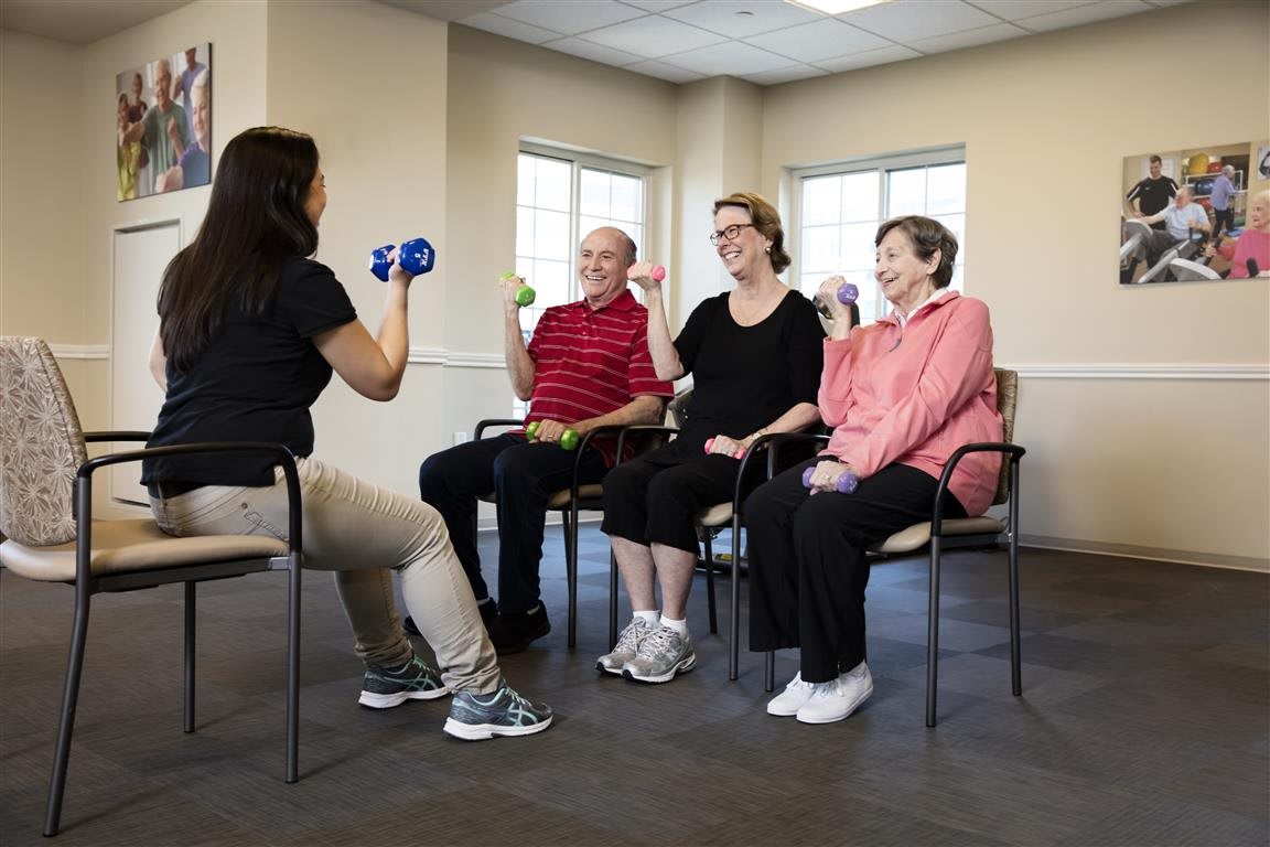 A group of seniors participating in a seated exercise class with an instructor.