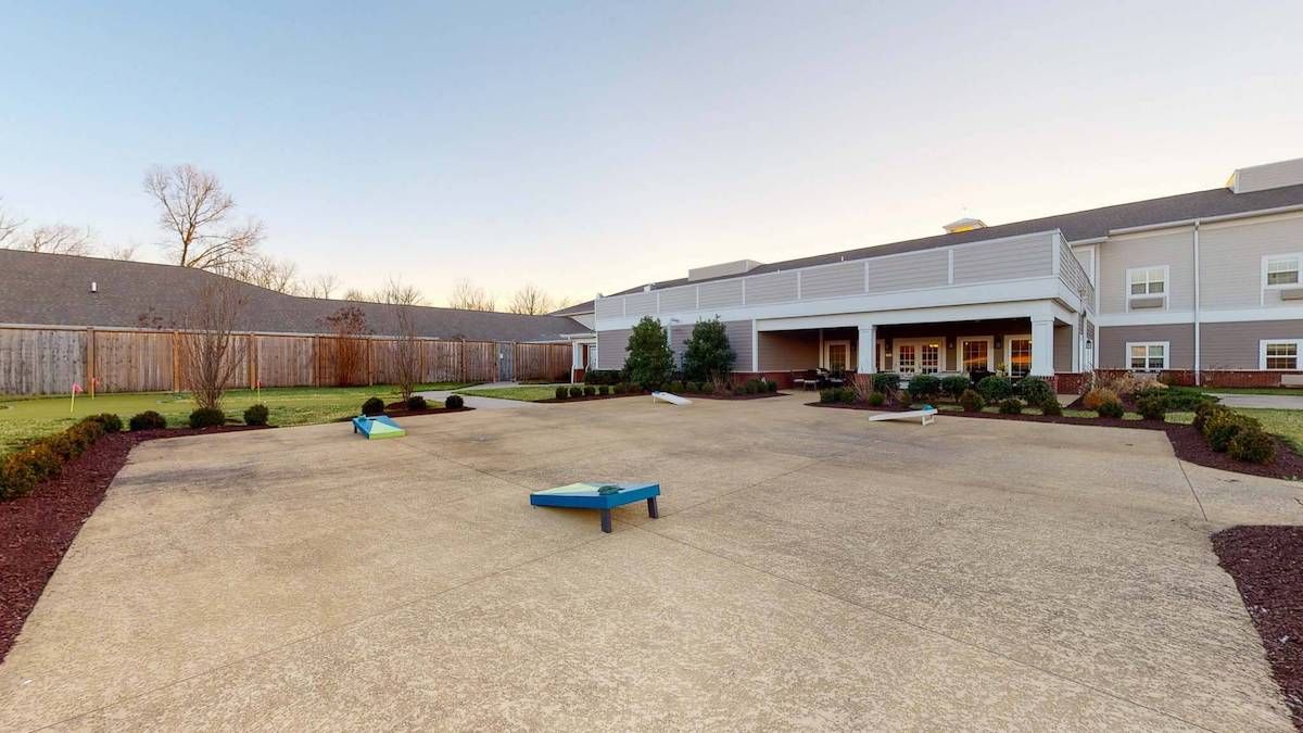 A spacious outdoor playground adjacent to a building, featuring play equipment and surrounded by a wooden fence.