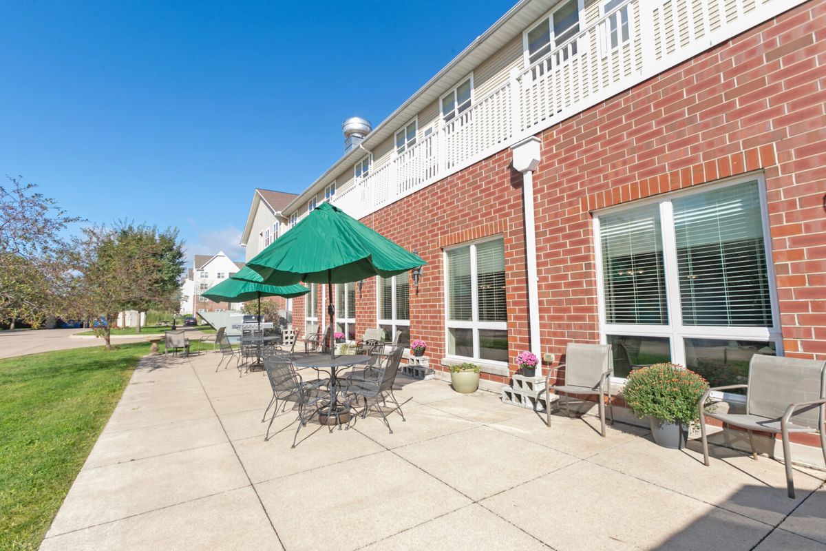 A sunny day on the patio with tables, chairs, and umbrellas outside a brick building.