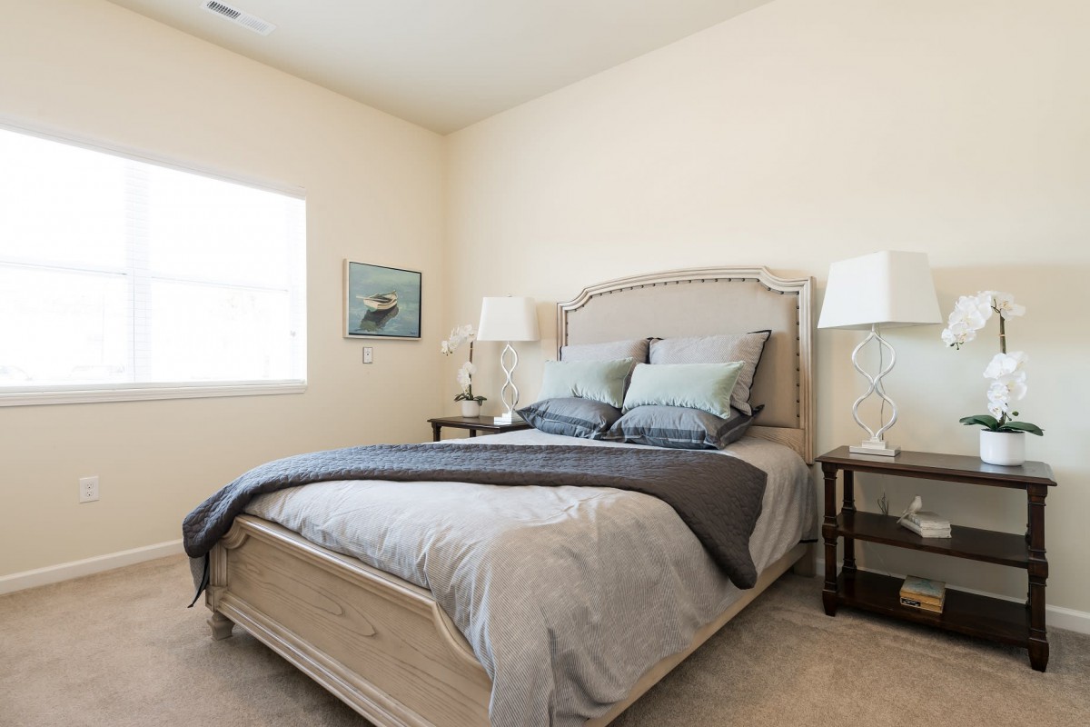 A cozy bedroom featuring a neatly made bed with neutral-colored bedding, flanked by two lamps on side tables.