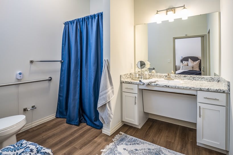 A bathroom with a blue shower curtain, a vanity with a mirror, and wooden flooring.