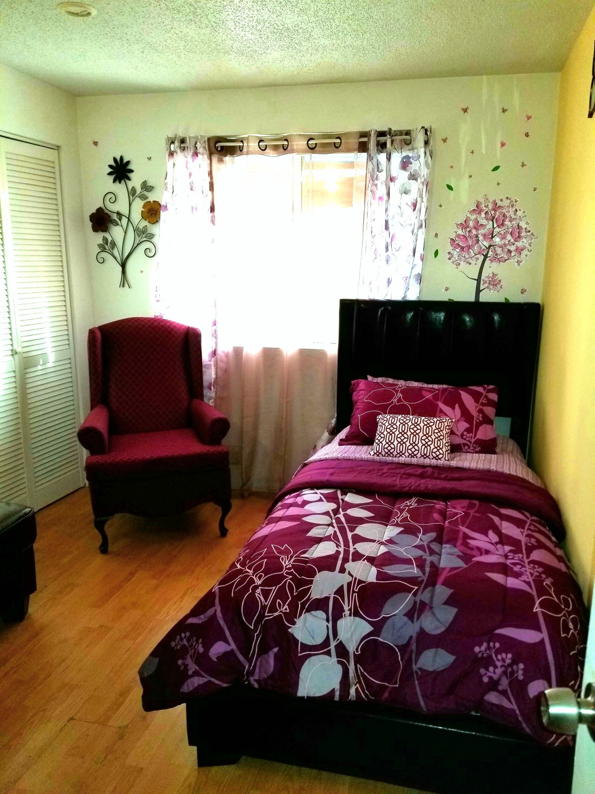 A cozy bedroom featuring a single bed with floral bedding and a maroon armchair.