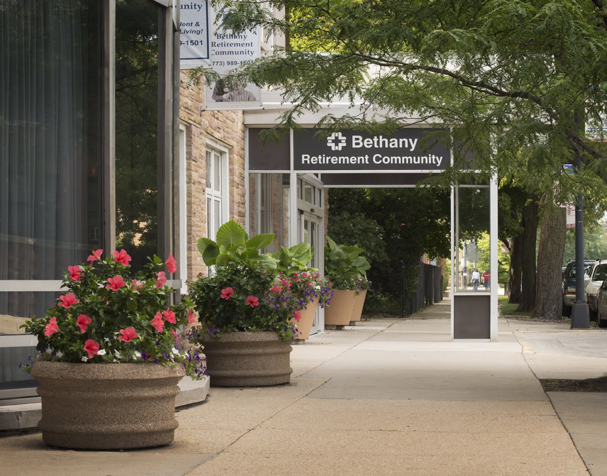 A welcoming entrance with planters full of flowers lining a sidewalk leading to a building.