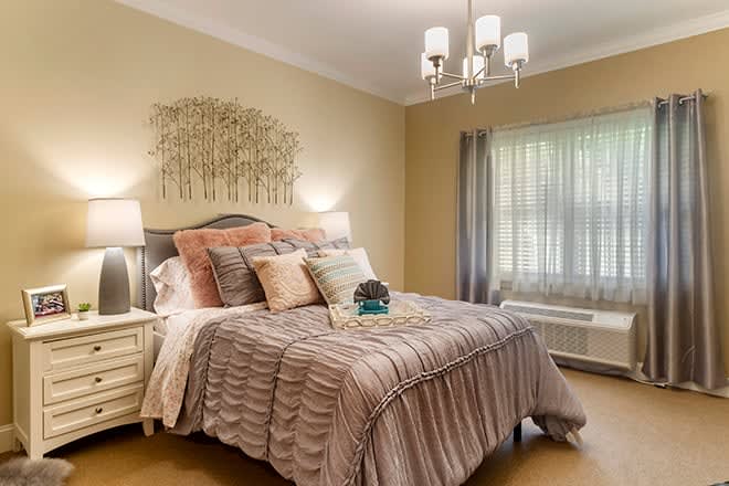 A cozy bedroom with elegant decor, featuring a neatly made bed adorned with multiple pillows and a stylish chandelier overhead.