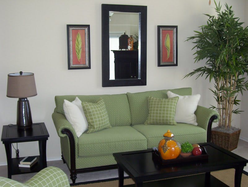 A cozy living room with a green sofa, decorative pillows, a wall mirror, and artwork. A coffee table with decorative items is in front of the sofa.