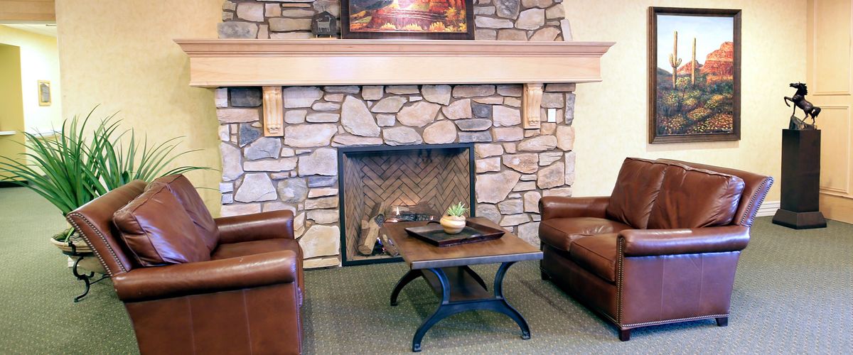 A cozy living room featuring a stone fireplace flanked by leather chairs and a central coffee table.