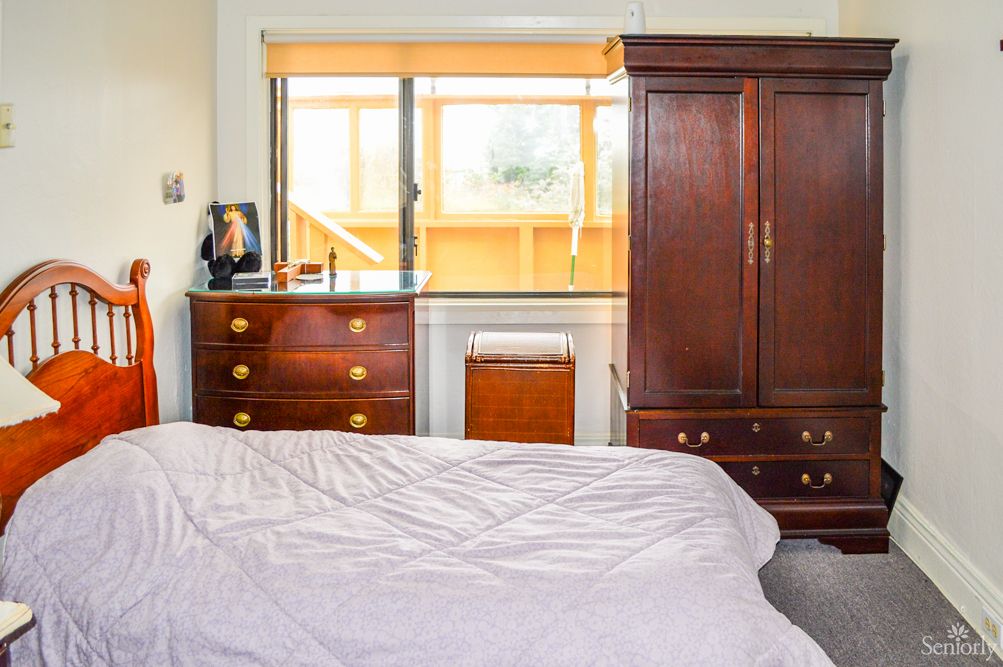 A cozy bedroom featuring a wooden wardrobe and dresser by a sunlit window.