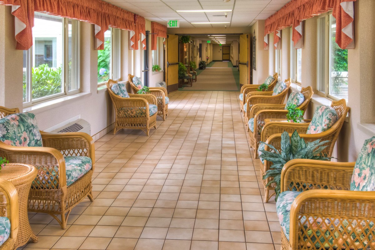 A long hallway with wicker chairs and a tiled floor, lined with windows.
