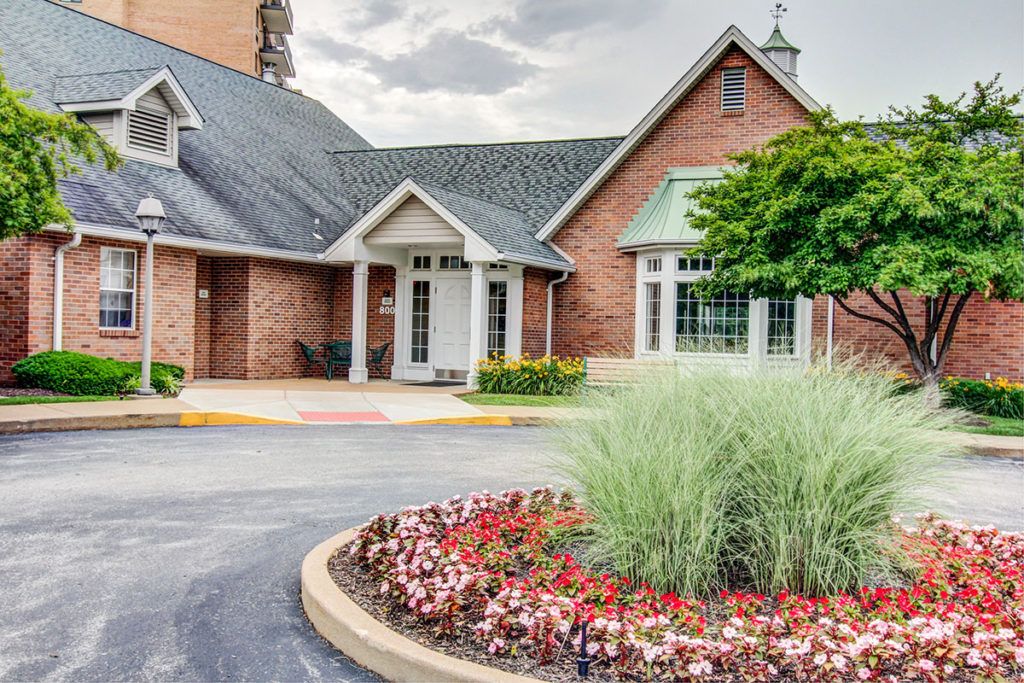 A charming brick house with a landscaped entrance and colorful flowers lining the driveway.
