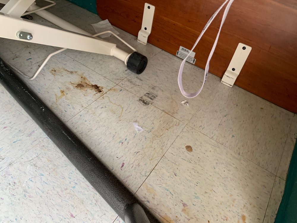 A messy floor area with signs of dirt and debris under a piece of furniture.