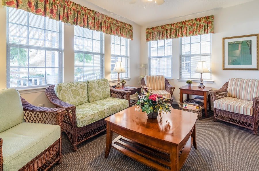 A cozy living room with wicker furniture, large windows, and decorative curtains.