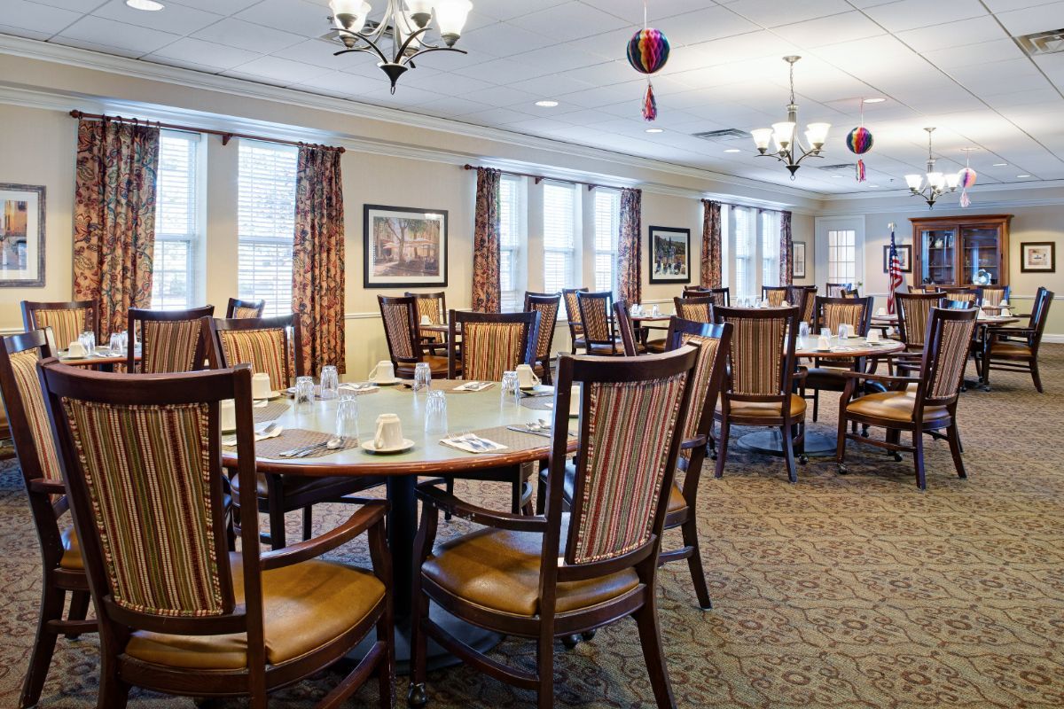 A spacious dining room with neatly arranged tables and chairs, featuring ceiling decorations and chandeliers.