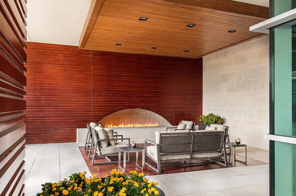 A modern outdoor patio with comfortable seating and a cozy fireplace, surrounded by stylish wood paneling.