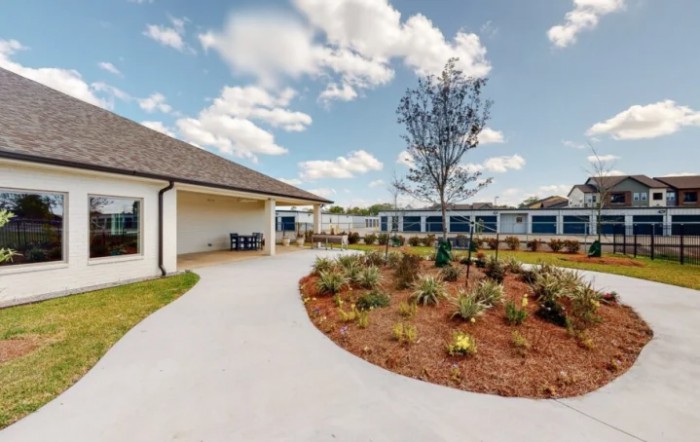 A landscaped garden with a pathway leading to a building under a cloudy sky.