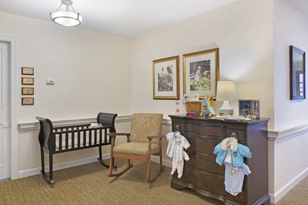 A cozy nursery room featuring a crib, a rocking chair, and a dresser adorned with children's clothing and artwork on the walls.