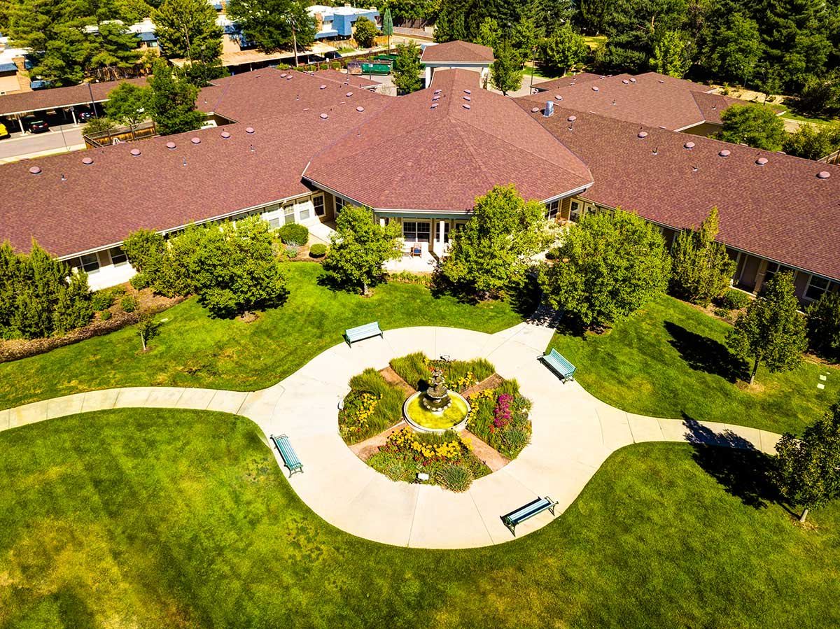 An aerial view of a building surrounded by lush greenery and a circular garden with benches.