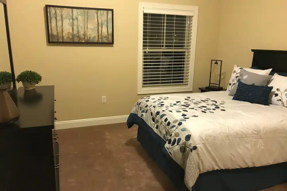 A neatly arranged bedroom with a bed, side table, lamp, and wall art.